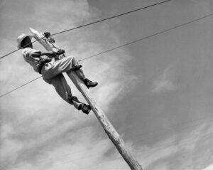 Sin título [Obrero trabajando en un tendido eléctrico montado sobre un poste de madera]
