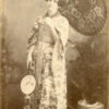 Dama retratada desde un plano general, vestida con kimono (yukata), traje típico japonés. Con su mano derecha sostiene una wagasa (sombrilla japonesa) y en la otra un abanico. Estudio Fotografía Artística, 1890.