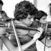 Niña y niño con violines. Ensayo. «Pioneros: Escenas de los primeros 5 años del Sistema de Orquestas Sinfónicas Juveniles e Infantiles de Venezuela». Caracas, Venezuela, ca. 1975-1980: © Antonio Huizi